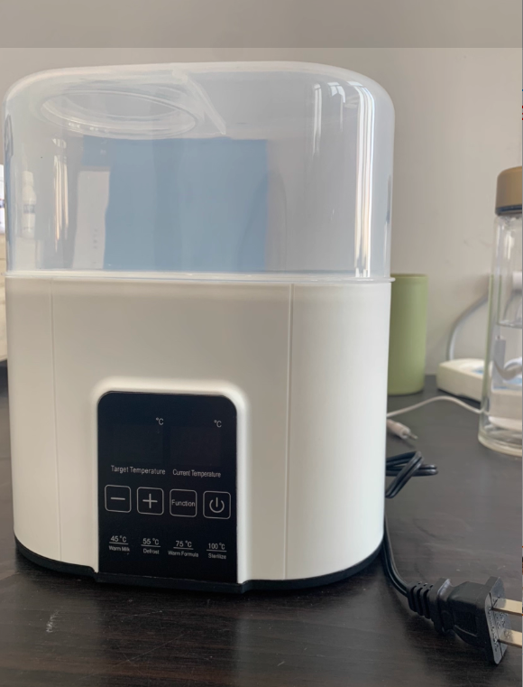White and clear baby bottle sterilizer on a dark surface with a blurred background