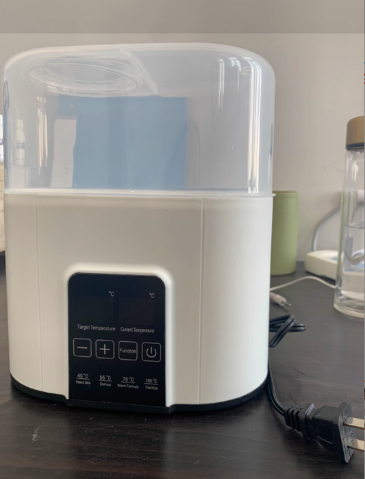White and clear baby bottle sterilizer on a dark surface with a blurred background