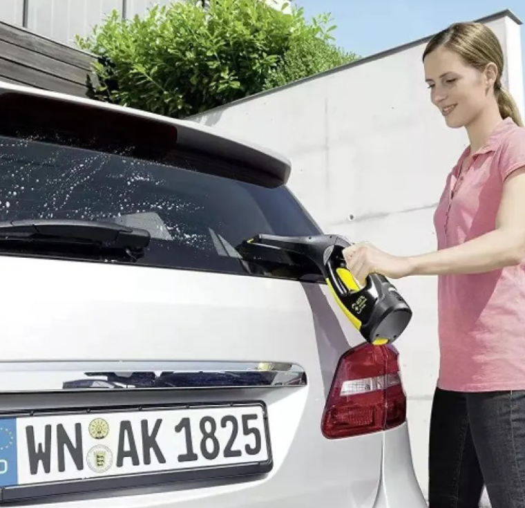 Woman using a car window cleaning tool on a car's rear window.