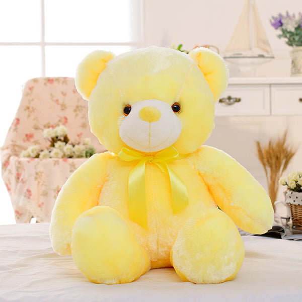 Yellow teddy bear plush toy on a bed with a blurred room background