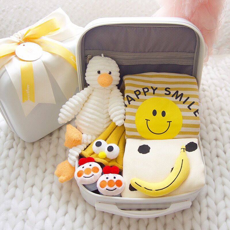 Small suitcase with plush toys including a duck, snowman, and banana with smiley face on a textured surface.