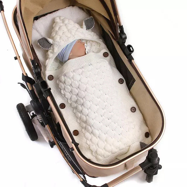 Baby swaddled in a white blanket inside a beige stroller on a white background