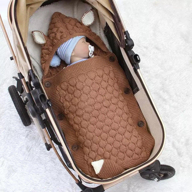 Baby in a brown knitted deer costume in a stroller on a white blanket