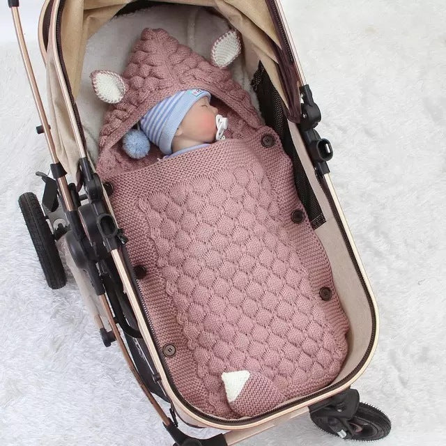 Baby in a stroller wrapped in a pink knitted blanket with animal ears.