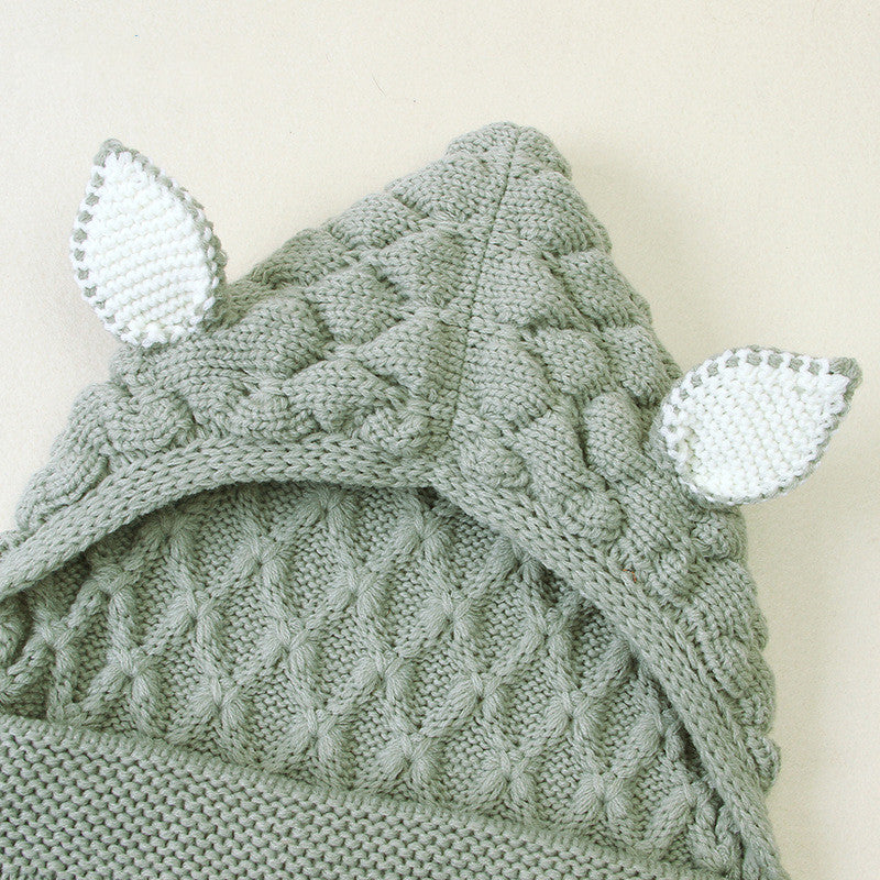 Knitted green baby hat with white ear accents on a light background