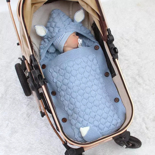 Baby swaddled in a blue knitted blanket with animal ears in a stroller.