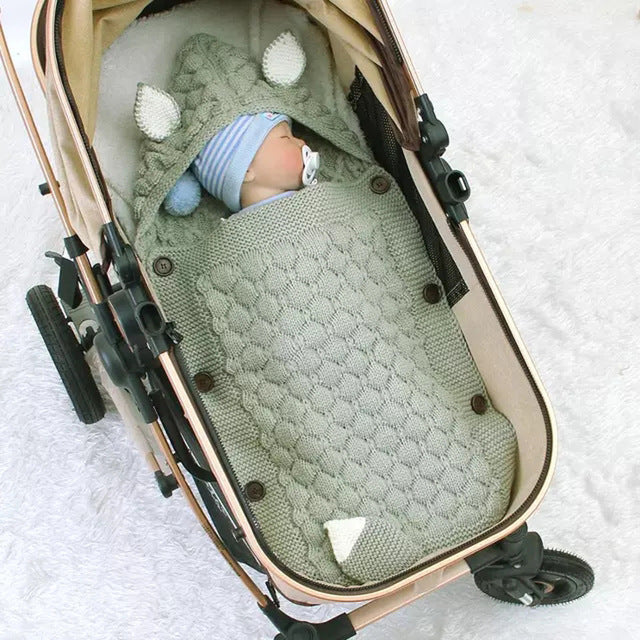 Baby wrapped in a green knitted blanket in a stroller on a white blanket