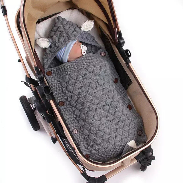 Baby in a gray knitted swaddle in a stroller on a white background