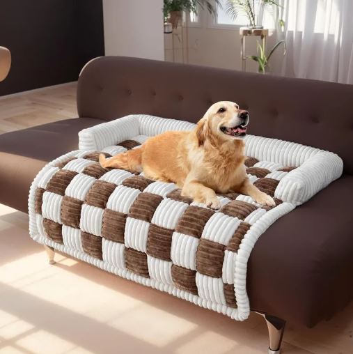 Dog lying on a checkered pet bed on a brown sofa in a bright room.