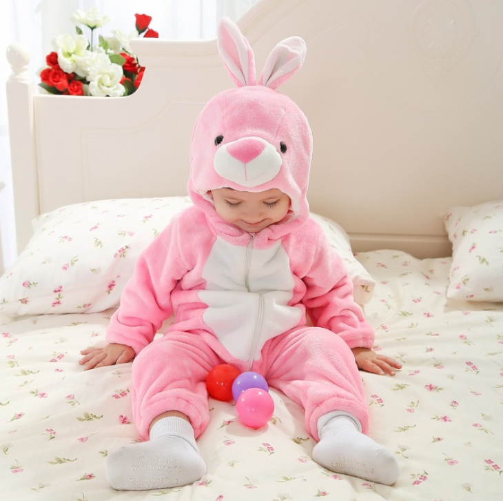 Child wearing a pink bunny onesie sitting on a bed with colorful balls.